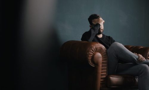 Man sits on a couch holding his head in distress