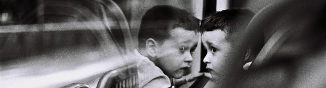 Black and white image of child looking at their reflection in a window