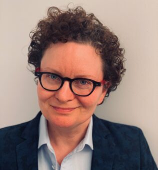A headshot of Dr. Carney smiling at the camera, wearing a light striped button-up with a navy blue blazer.