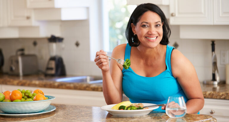 Woman is smiling while eating a healthy meal in the kitchen