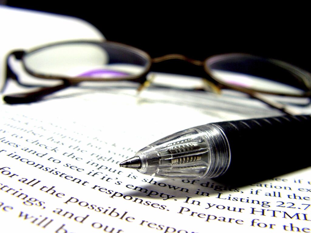A pen and pair of glasses, on top of an open book.